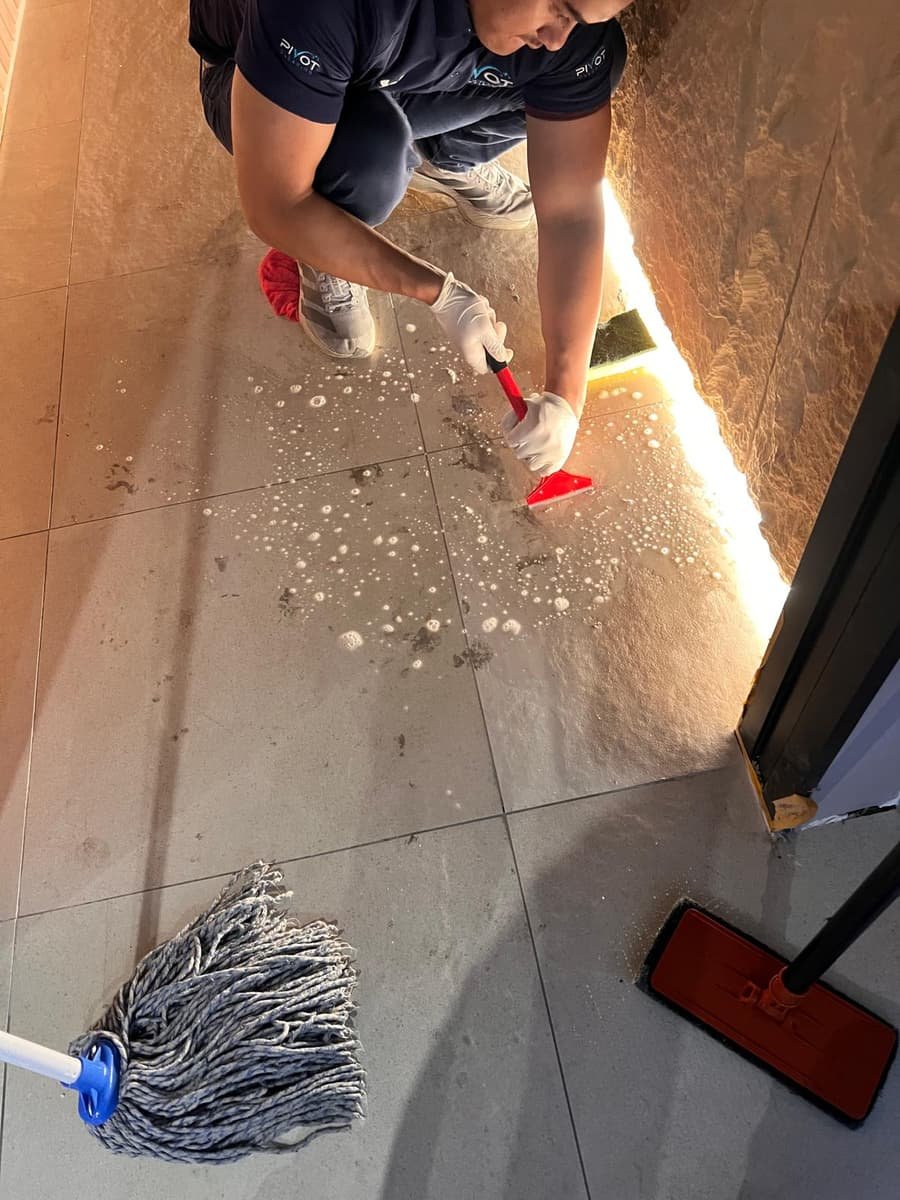 Pivot Cleaning team member hand-scrubbing tile and grout — detail clean in progress